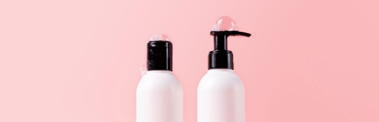 two white bottles of shampoo and conditioner arranged in front of pink wall