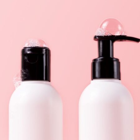 two white bottles of shampoo and conditioner arranged in front of pink wall