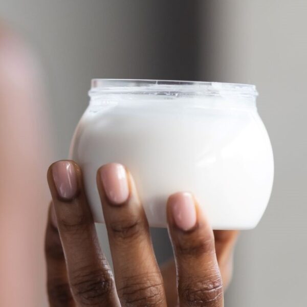 close up image of woman's hand holding a container of white body lotion