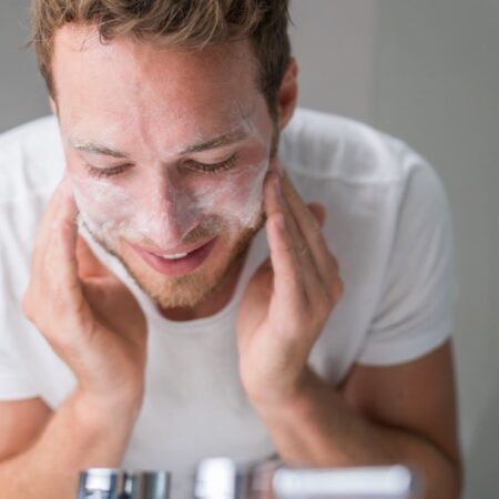 man washes his face with a facial cleanser standing over a sink