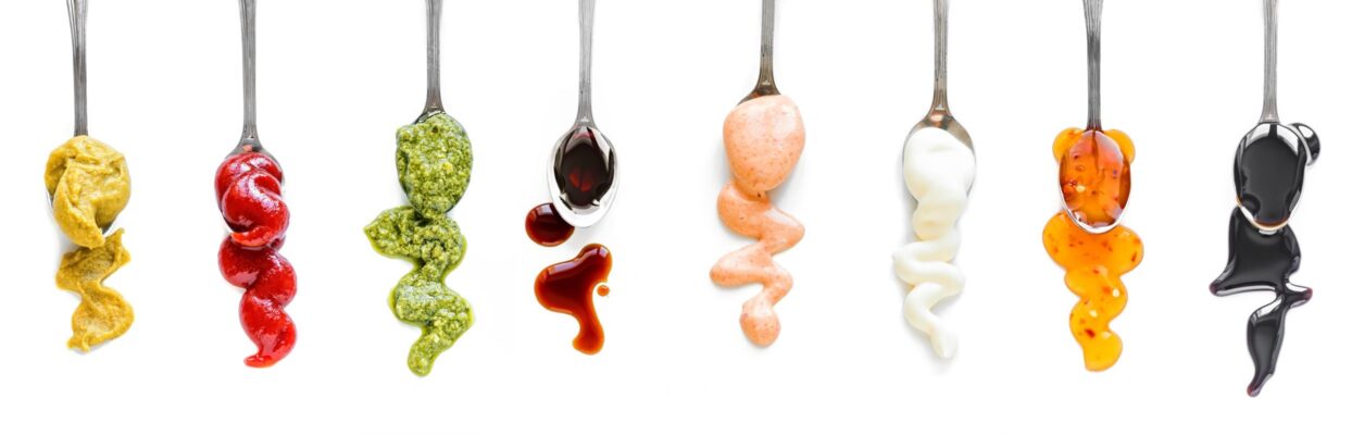 eight spoons in a row drizzling sauce and condiments used in food products