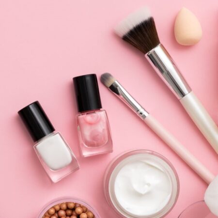 makeup brushes, nail polish and facial cream arranged on pink background
